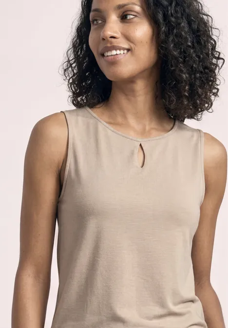 Een vrouw met krullend haar draagt een beige mouwloze top met een klein splitje bij de halslijn.