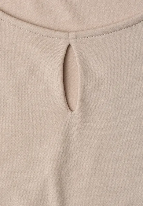 Close-up van een beige top van zacht materiaal met een kleine druppelvormige uitsnijding bij de hals.