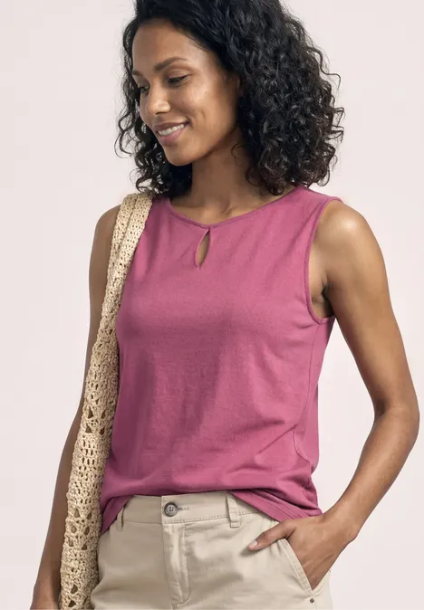 Persoon in roze mouwloze top, beige broek, gehaakte tas over schouder, krullend haar, wazig gezicht.