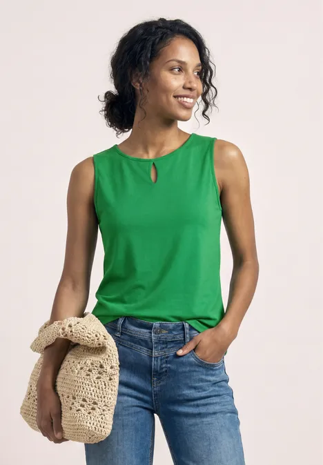 Vrouw in groen mouwloos topje en jeans met een beige gehaakte tas.