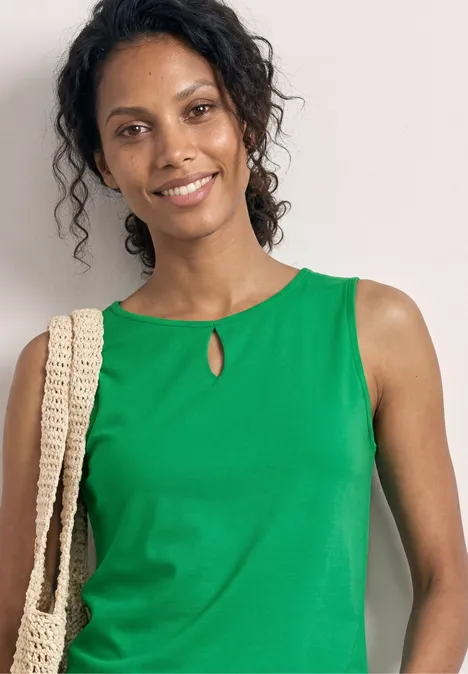 Vrouw in groen mouwloos topje met gehaakte schoudertas voor een witte muur