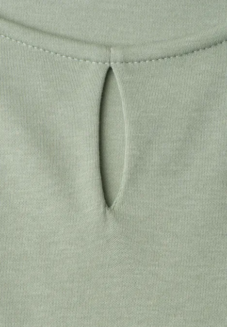 Nahe Aufnahme eines hellgrünen Stoffes mit kleiner, ovaler Öffnung und Ziernaht.