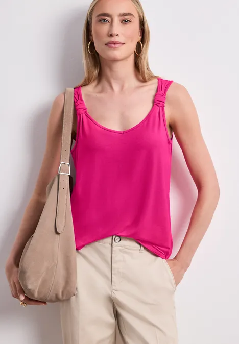 Frau in pinkem Top, beiger Hose und mit beiger Schultertasche.