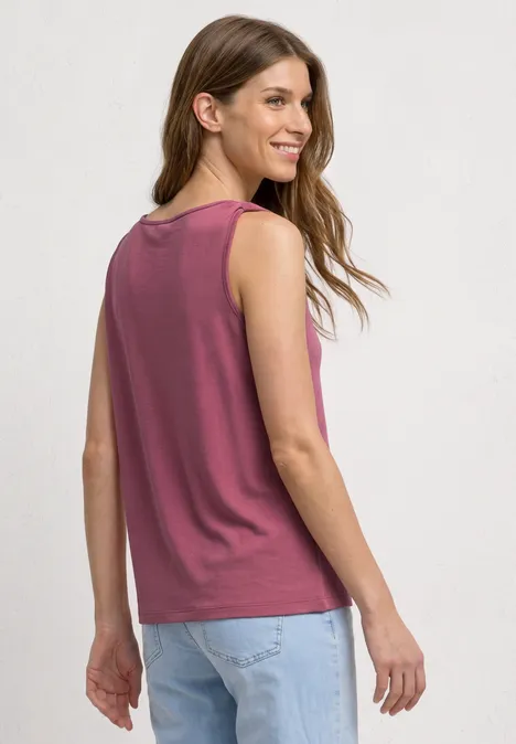 Vrouw van achteren in een mouwloos bordeaux topje en lichtblauwe jeans, losse pasvorm en los haar.