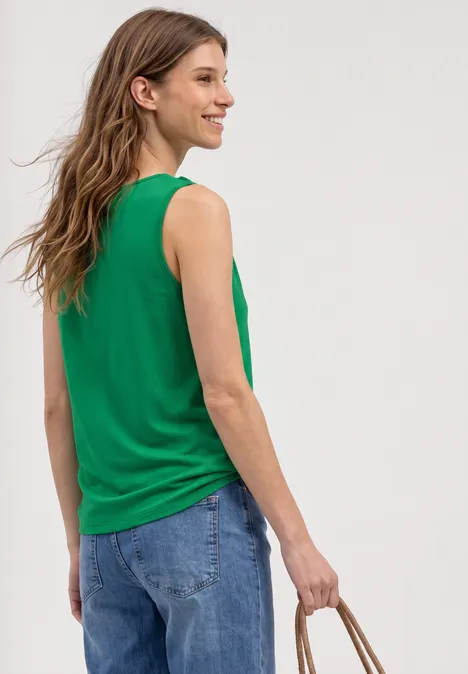 Person von hinten in grünem ärmellosen Top und blauen Jeans, hält einen geflochtenen Strohkorb.