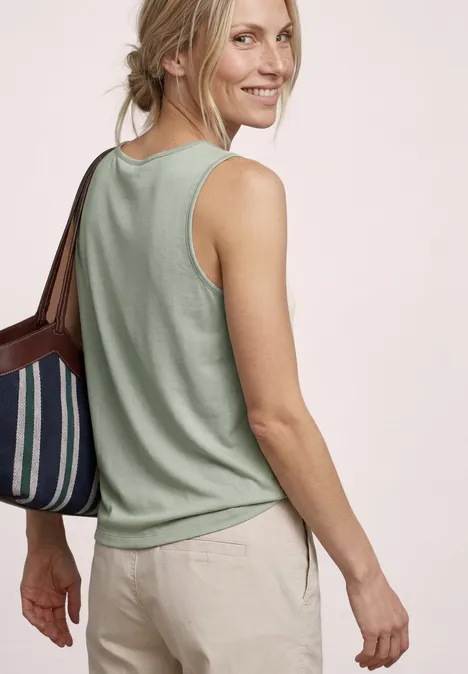 Vrouw van achteren in groene tanktop, beige broek en gestreepte handtas.