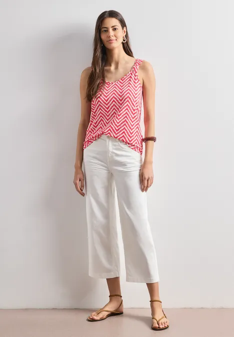 Top mit V-Neck und Knotendetail salsa red Frau trägt rosa Chevron-Top, weiße Culottes und Sandalen, vor schlichtem weißen Hintergrund.