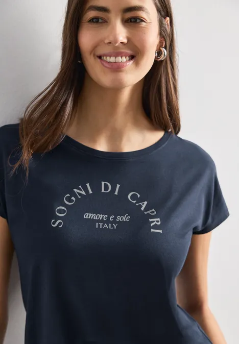 Dropped Shoulder Shirt mit Rundhals deep blue Junge Frau mit braunen Haaren lächelt und trägt dunkelblaues T-Shirt mit Aufschrift 'Sogni di Capri'.