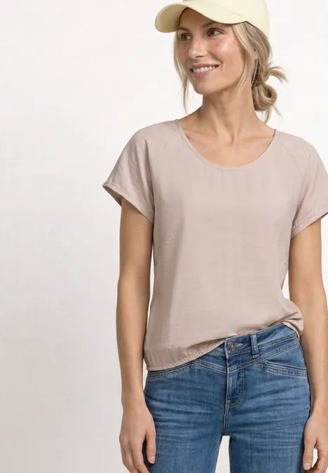 Jeune femme portant un t-shirt beige et un jean bleu sur fond neutre.