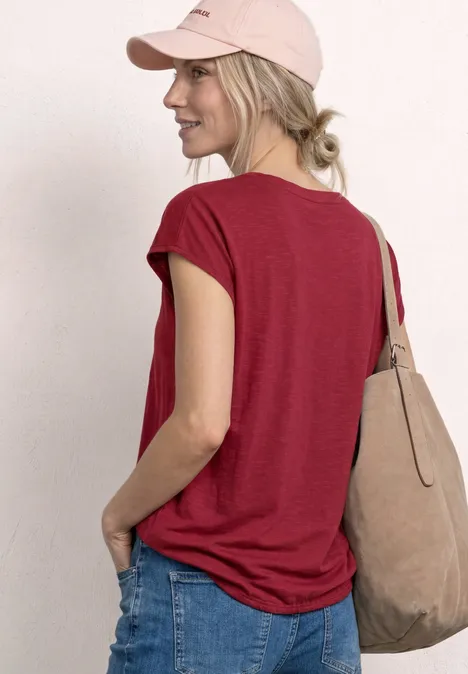 Vrouw van achteren in rood shirt, spijkerbroek, roze pet en beige tas.