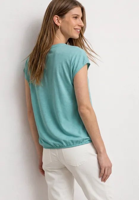 Une femme vue de dos porte un t-shirt vert et un pantalon blanc.