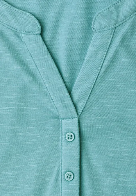 Gros plan sur un T-shirt turquoise à col en V avec trois boutons.