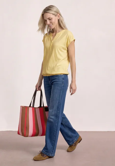 Dropped Shoulder Shirt mit Split Neck soft yellow Frau in gelbem Oberteil und blauen Jeans trägt bunte gestreifte Tasche.
