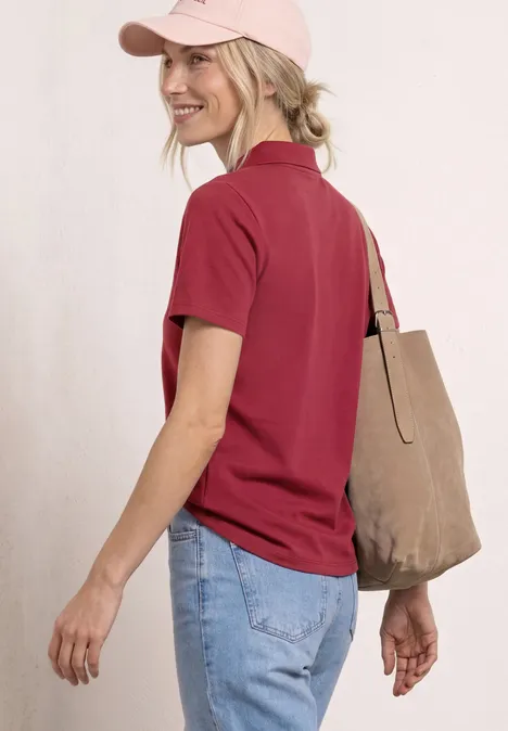 Vrouw van achter in een rood poloshirt, blauwe jeans, roze pet en beige stoffen tas.
