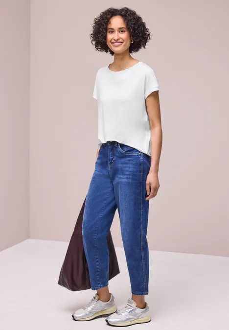 Shirt met ronde hals en decoratieve tape off white Een persoon draagt een wit t-shirt, blauwe jeans, sneakers en houdt een tas vast in een neutrale ruimte.