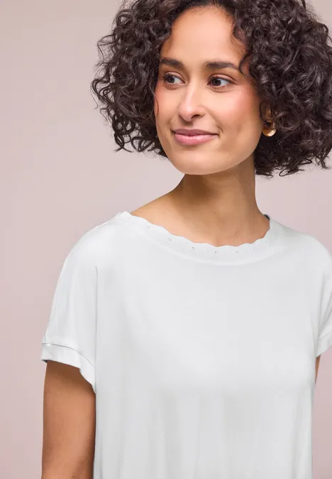 Shirt met ronde hals en decoratieve tape off white Persoon met krullend haar draagt een wit T-shirt met gegolfde halslijn en opgerolde mouwen.