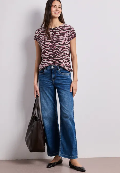 Vrouw draagt zebraprint t-shirt, wijde jeans, zwarte ballerina’s en grote zwarte shopper.