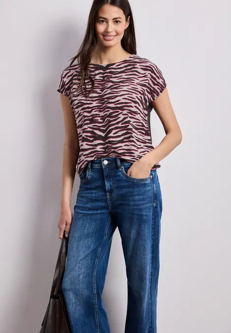 Vrouw met zebraprintshirt, blauwe jeans en zwarte tas tegen lichte achtergrond.