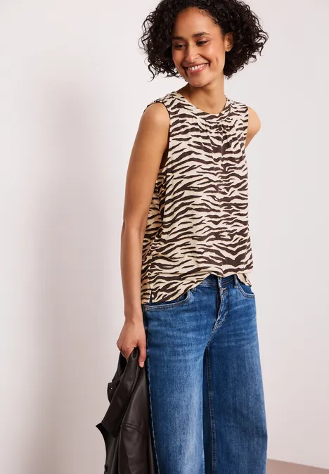 Moderne Frau trägt zebra-gestreiftes Top, weite Jeans und hält schwarze Tasche.