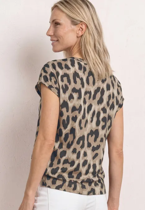 Frau von hinten in beiger Leopardenmuster-Bluse und weißer Hose vor hellem Hintergrund.