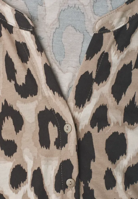 Nahaufnahme eines beigen Kleidungsstücks mit schwarzem Leopardenmuster und sichtbaren Knöpfen.