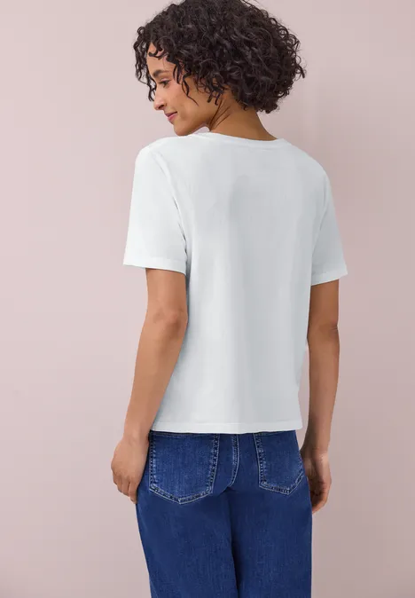 Een vrouw van achteren in wit T-shirt en blauwe jeans, tegen een pastelroze achtergrond.