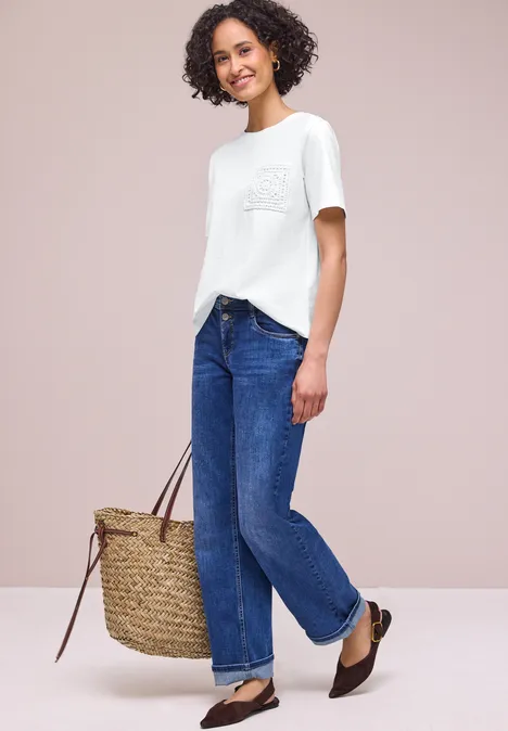 Vrouw in wit t-shirt, blauwe jeans en bruine ballerina's met grote rieten tas.