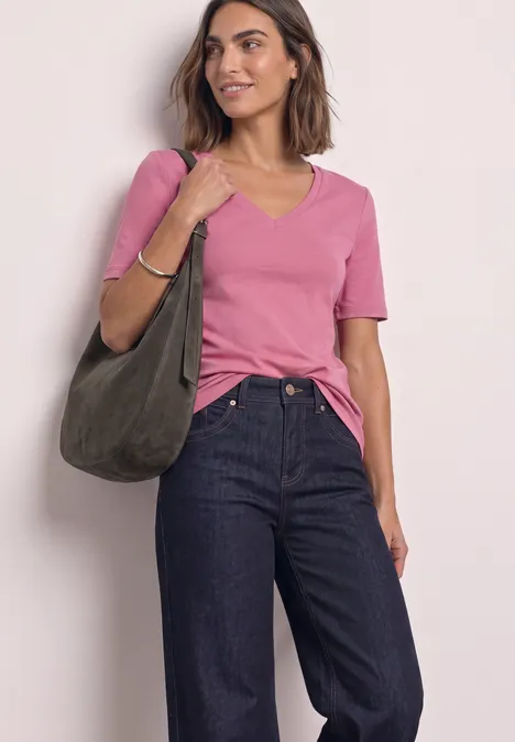 Frau trägt rosa T-Shirt, dunkelblaue Jeans und hält eine olivgrüne Tasche.