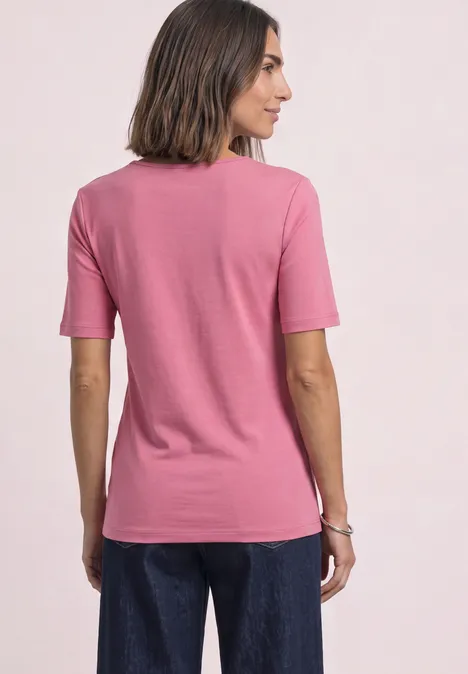 Frau von hinten in rosa T-Shirt und blauen Jeans, Arme locker an den Seiten.