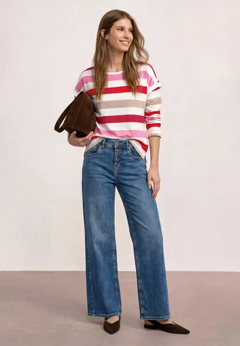 Vrouw in roze-wit gestreepte trui, wijde jeans, zwarte pumps en bruine schoudertas.