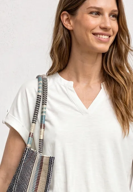 Shirt met gespleten hals en knoopdetails off white Vrouw in wit V-hals T-shirt draagt gestreepte schoudertas.