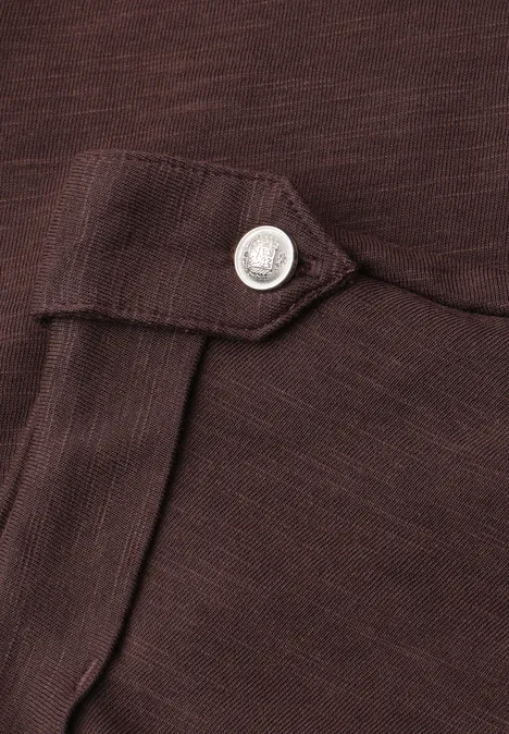 Detailaufnahme eines braunen Kleidungsstücks mit Stoffklappe und silbernem Druckknopf.