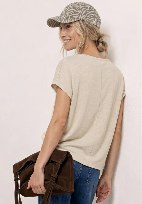 Vrouw van achteren in een casual outfit: beige T-shirt, jeans, pet en bruine schoudertas.
