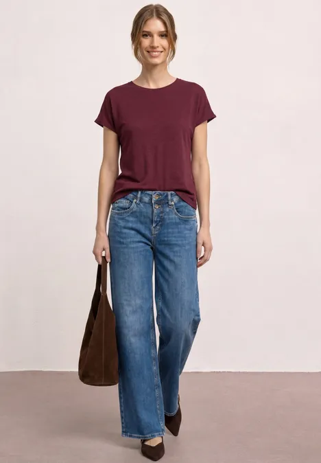 Vrouw draagt een bordeauxrood T-shirt, wijde spijkerbroek, zwarte laarzen en schoudertas.