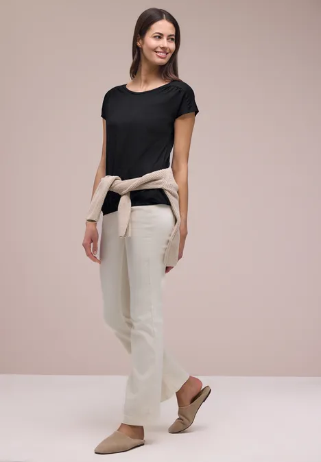 Vrouw in zwart T-shirt, lichte broek, trui om de taille geknoopt en sandalen.