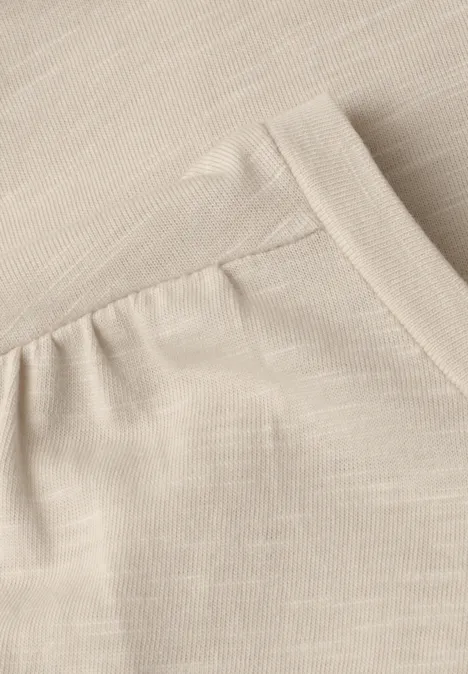 Close-up van een beige stof met een ingestikte zak en zichtbare naden.