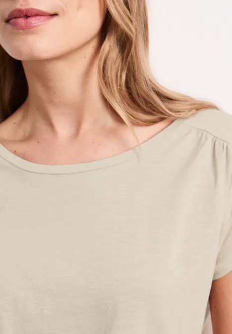 Close-up van een vrouw in een beige T-shirt met ronde hals en korte mouwen.