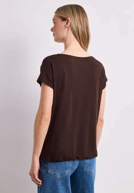 Vrouw van achteren in een bruin T-shirt en blauwe spijkerbroek voor een lichte achtergrond.