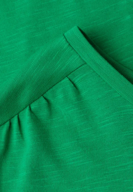 Close-up van een groen geribd T-shirt met V-hals en lichte plooien onder de kraag.