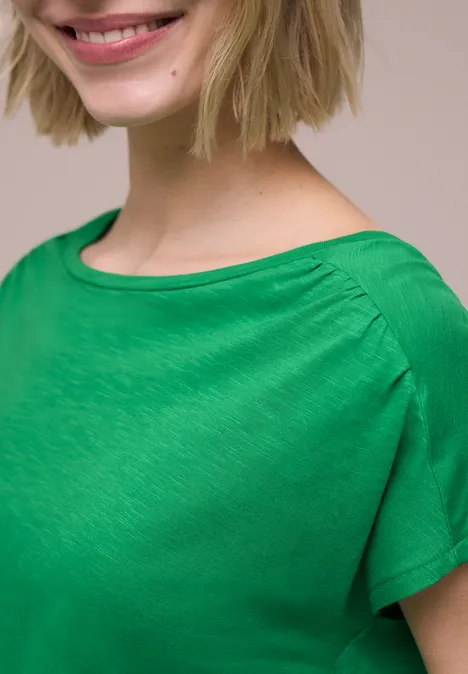 Nauw portret van vrouw in groen shirt met een subtiele glimlach.