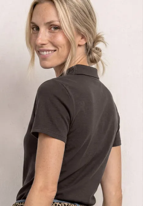 Vrouw in zwart T-shirt met korte mouwen, blond haar in knot, kijkend over haar schouder.