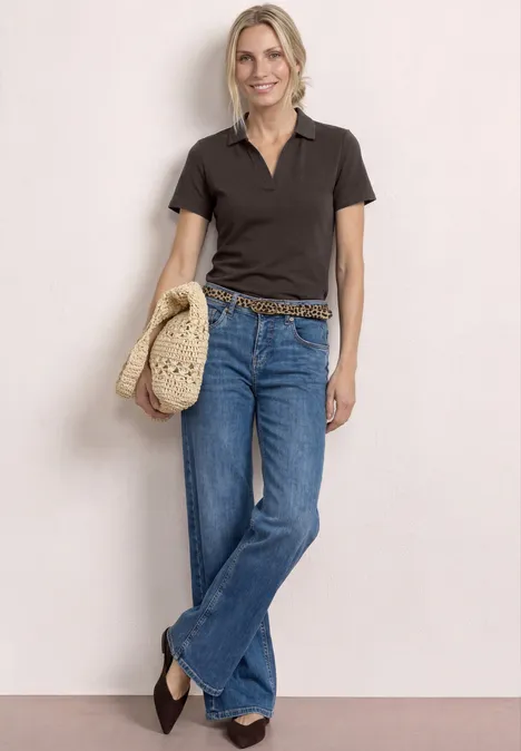 Vrouw in donker poloshirt, uitlopende jeans, gevlochten riem en strohoed.