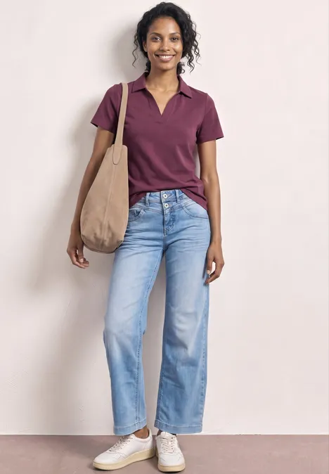 Persoon draagt paars poloshirt, lichtblauwe spijkerbroek, witte sneakers en een beige tas.