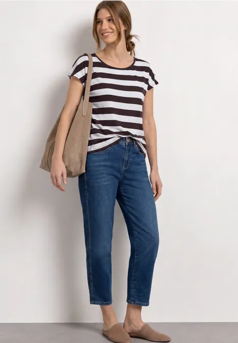 Frau in gestreiftem T-Shirt, blauen Jeans, brauner Tasche und flachen Schuhen vor neutralem Hintergrund.