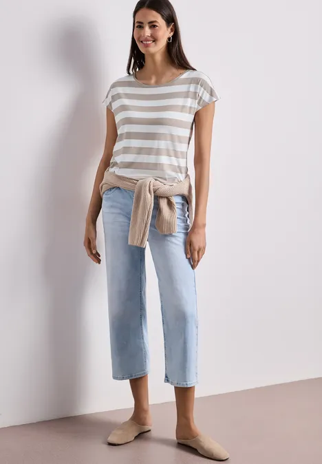 Frau trägt gestreiftes T-Shirt, helle Jeans, Sweatshirt um die Taille und bequeme Slipper.