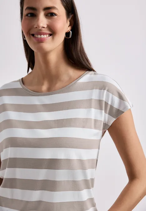 Eine lächelnde Frau in einem beige-weiß gestreiften T-Shirt vor hellem Hintergrund.