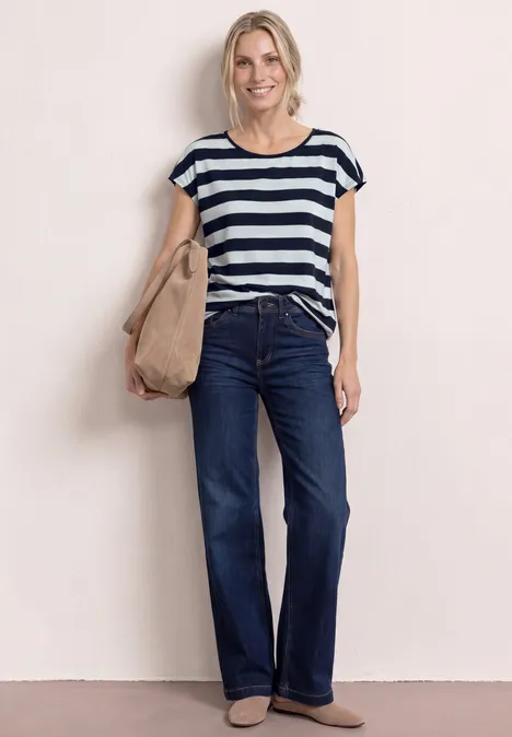 Vrouw met marine-wit gestreept T-shirt, donkerblauwe jeans, beige schoudertas en puntige platte schoenen.