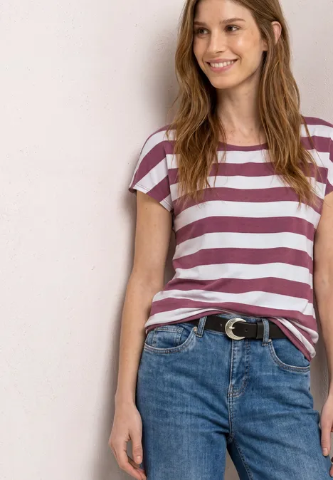 Shirt met korte mouwen, ronde hals en print dark clouded blush Vrouw met paars-wit gestreept T-shirt en een spijkerbroek met riem.