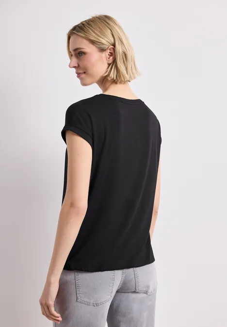 Frau von hinten in schwarzem T-Shirt und hellen Jeans vor weißem Hintergrund.