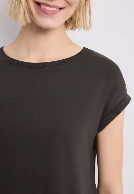 Nahe Aufnahme einer lächelnden Frau in schwarzem T-Shirt vor hellem Hintergrund.